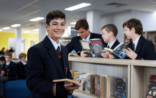 A photo of a secondary school student smiling with a book while his three friends in the background also read